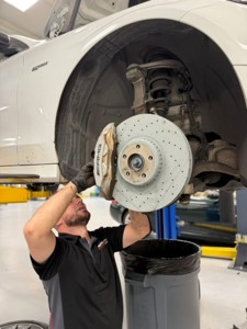 Autoscope technician removing a worn front brake rotor and AMG caliper from a Mercedes on a lift